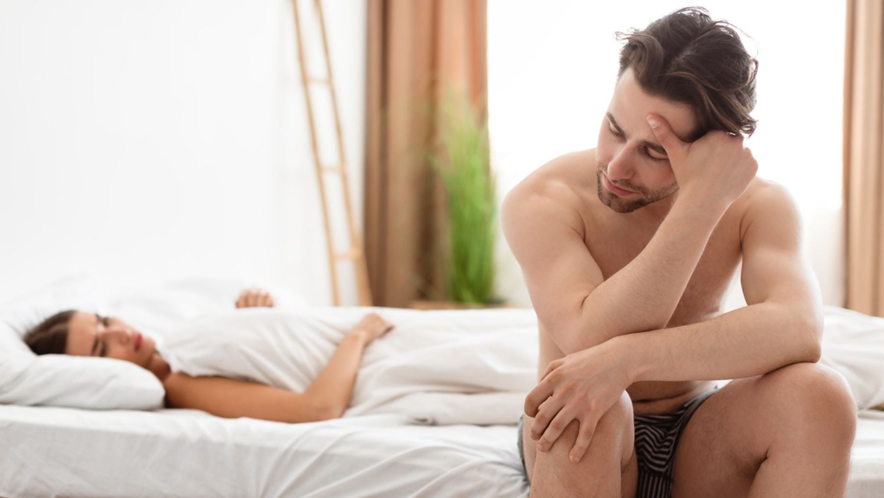 Un hombre con gesto serio sentado en el borde de la cama.